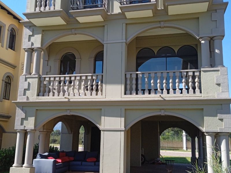 A multi-story residential facade featuring arched architectural details, stone balustrades on multiple balconies, and a covered ground-level patio area.