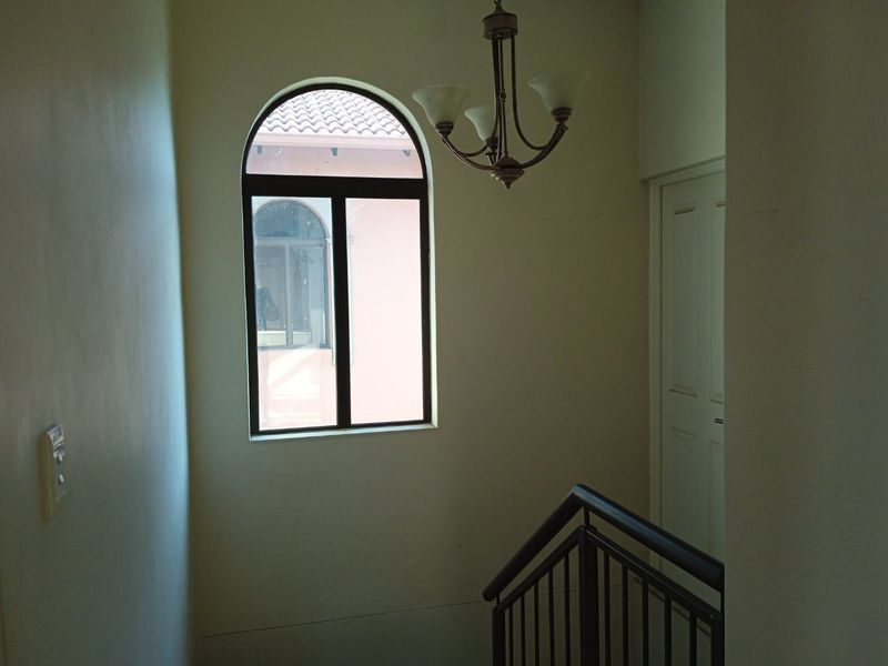 A bright hallway featuring an arched window, a metal staircase railing, and a classic chandelier, providing a clean and functional transition space.