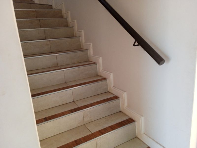 A clean, well-maintained staircase featuring tiled steps with metal nosing and a modern wall-mounted handrail.