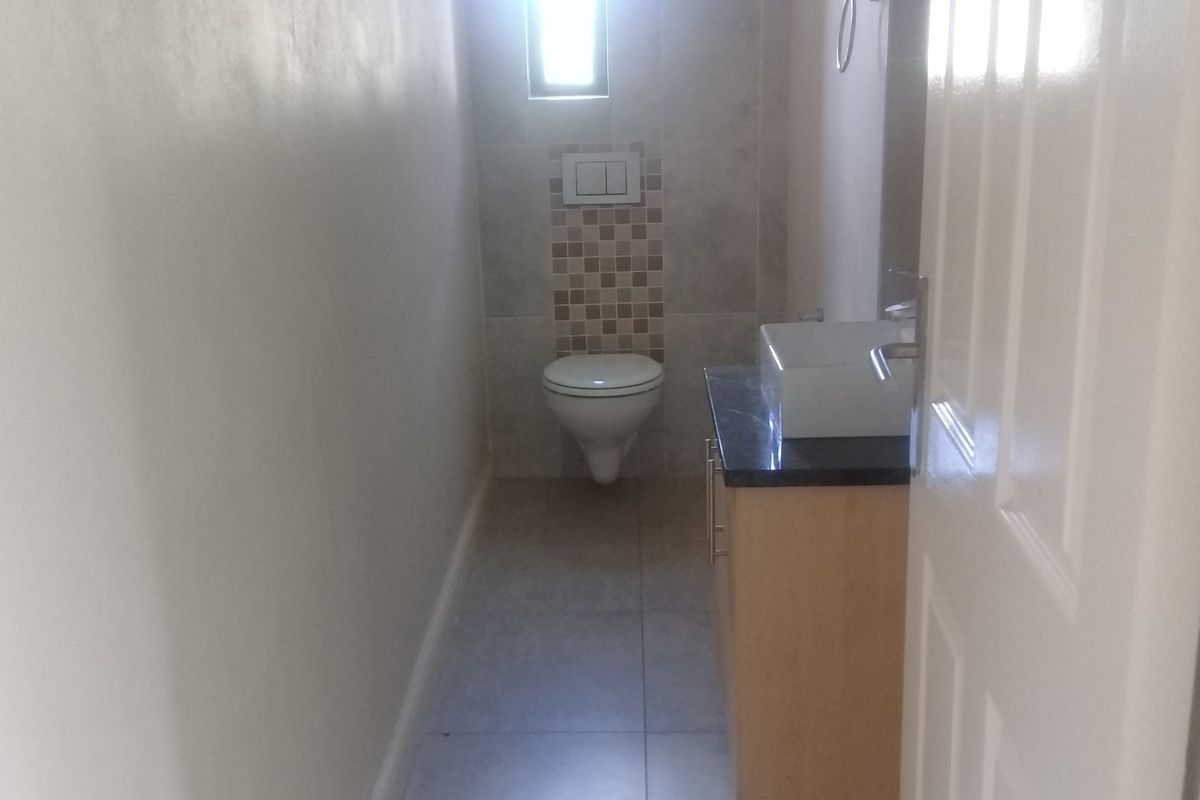 A compact bathroom featuring a wall-mounted toilet, a modern vessel sink set on a vanity cabinet, and neutral floor and wall tiling.
