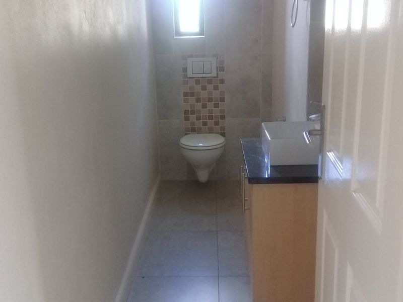 A compact bathroom featuring a wall-mounted toilet, a modern vessel sink set on a vanity cabinet, and neutral floor and wall tiling.