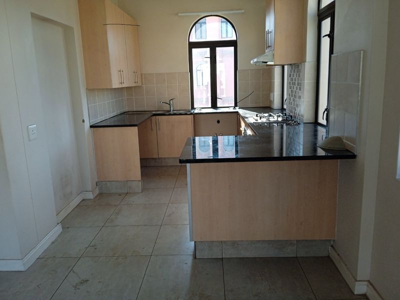 A functional kitchen featuring light wood cabinetry, dark granite countertops, a gas hob, and tiled flooring, offering a clean canvas for updates.