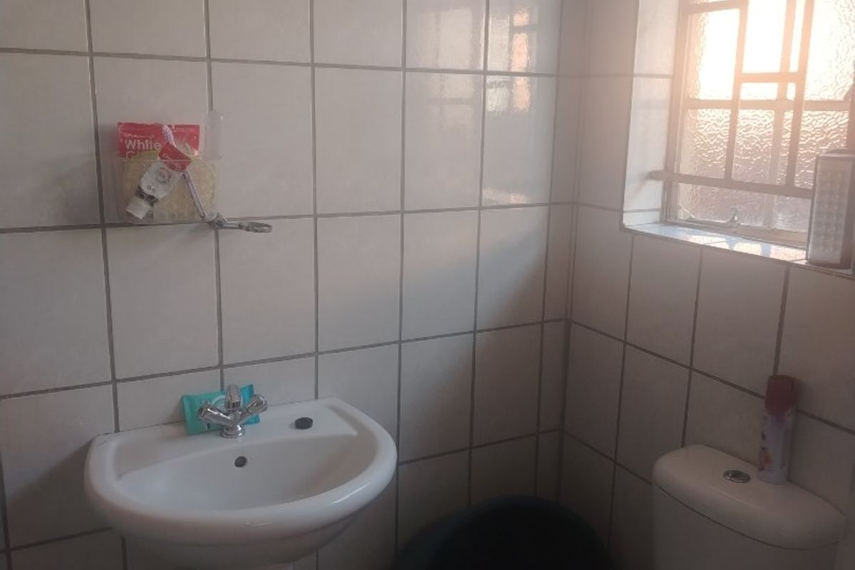 A compact bathroom featuring a pedestal basin, toilet, and tiled walls with a security window grille.