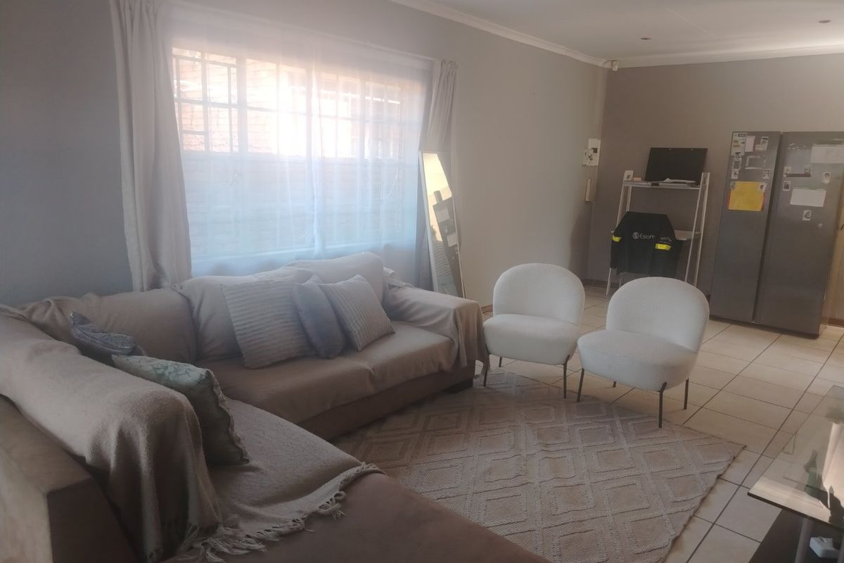 A neutrally painted living room featuring tiled flooring and a large window with security bars, offering a functional and well-lit living space.