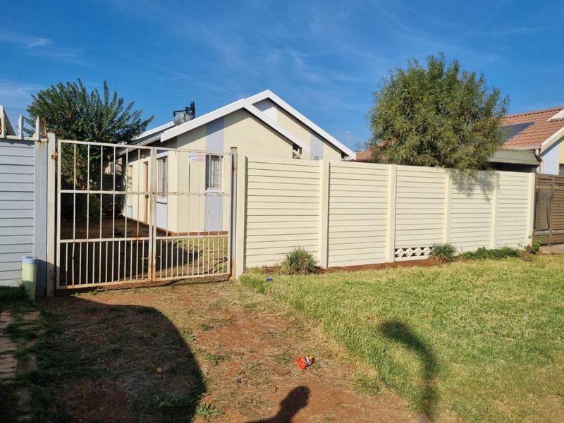 Front view of the property featuring a precast concrete boundary wall, metal driveway gate, and a solar water heater installed on the tiled roof.