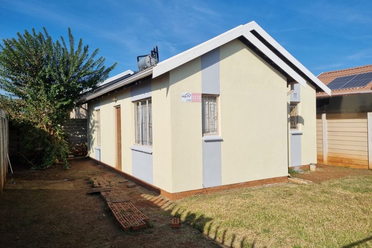 Rear view of a detached house featuring a solar geyser, plastered exterior walls, and secure window burglar bars set within a private garden area.