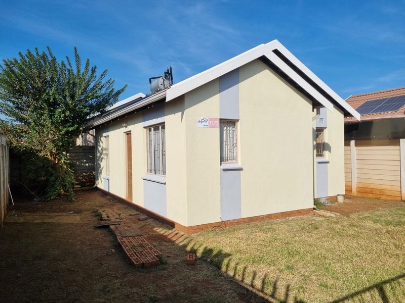 Rear view of a detached house featuring a solar geyser, plastered exterior walls, and secure window burglar bars set within a private garden area.