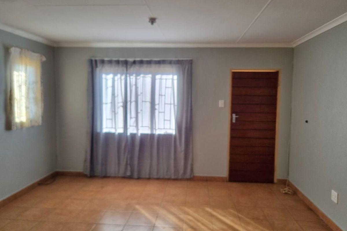 A vacant living room featuring neutral wall paint, tiled flooring, and a timber door, offering a clean canvas for interior design.