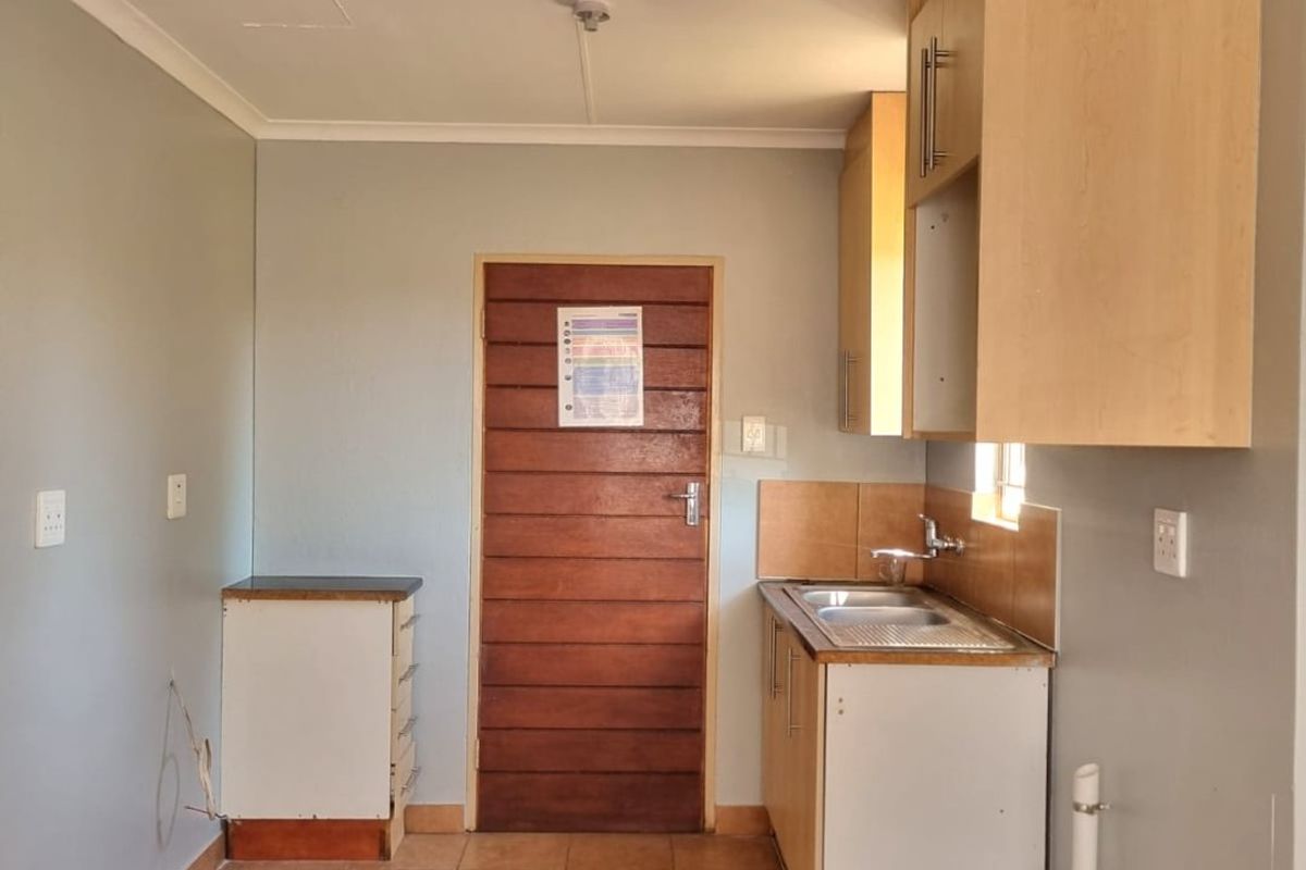 A compact, empty kitchen area featuring basic built-in cabinetry, a stainless steel sink, and tiled flooring, ready for renovation or functional updates.