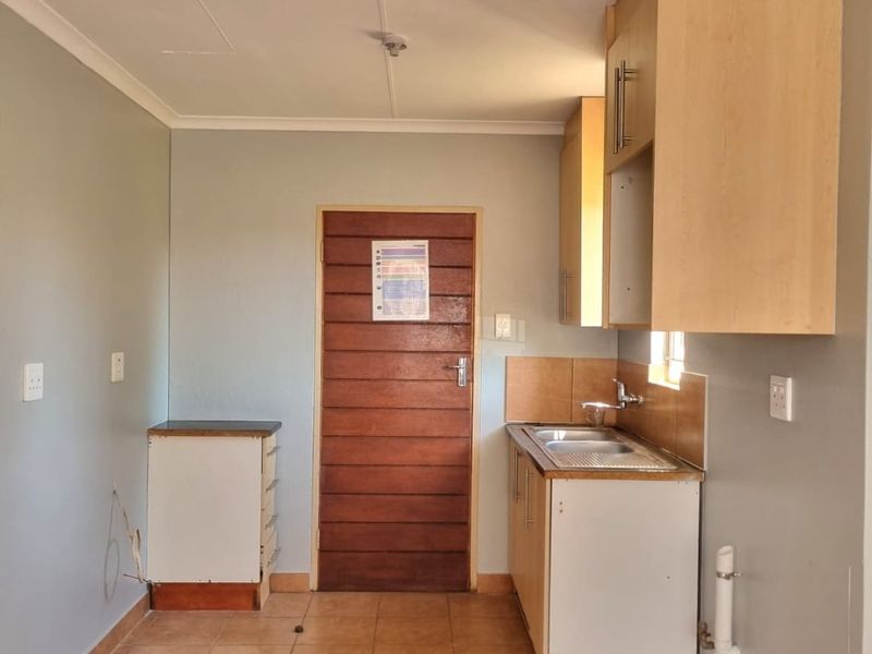 A compact, empty kitchen area featuring basic built-in cabinetry, a stainless steel sink, and tiled flooring, ready for renovation or functional updates.