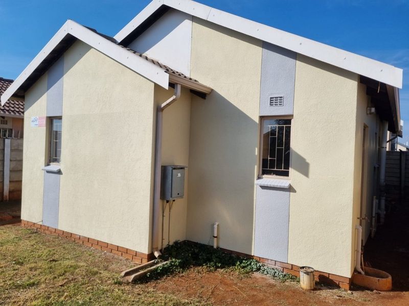 Rear exterior view of the house featuring plastered walls, tiled roof, and functional drainage systems with security bars on windows.