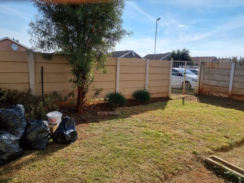 A rear garden area featuring a precast concrete boundary wall and a metal security gate, providing a private outdoor space.