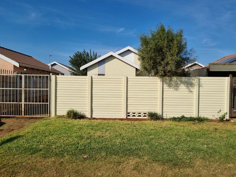 A well-maintained rear garden featuring a precast concrete boundary wall, a metal access gate, and a neat lawn area.