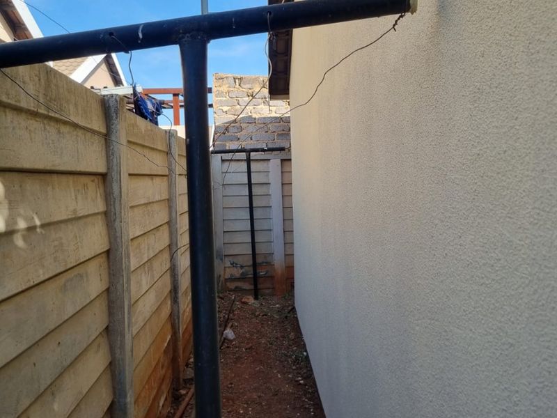 A narrow side passage of the property featuring a precast concrete boundary wall, plastered exterior wall, and a mounted satellite dish.