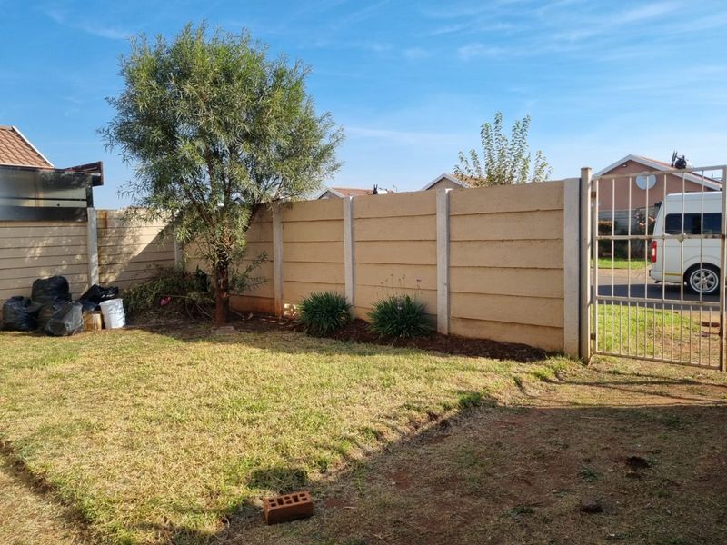 A private rear garden area featuring a precast concrete boundary wall, a metal security gate, and a grass lawn.
