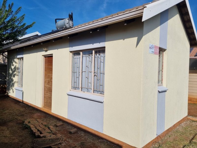 A side view of a single-story residential house featuring plastered walls, a tiled roof, and a solar water heating system.