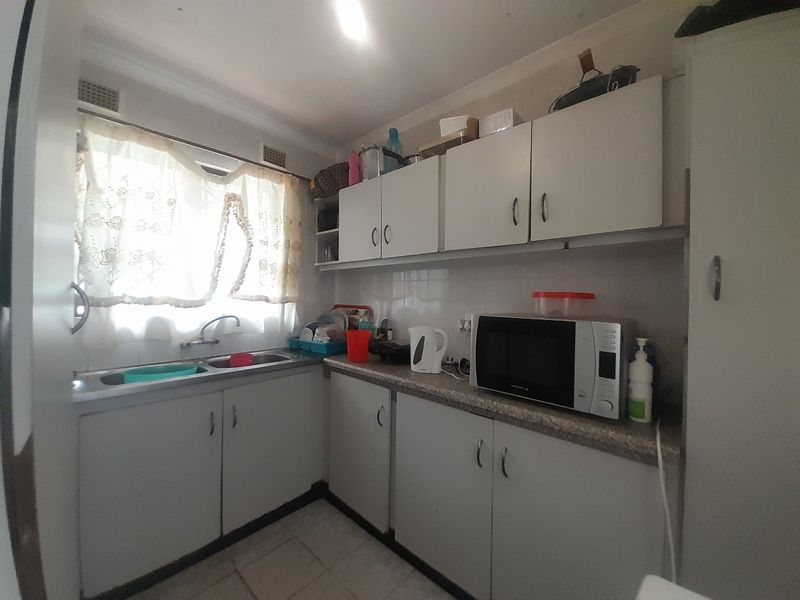 A functional kitchen featuring built-in cabinetry, laminate countertops, a stainless steel sink, and tiled finishes, offering potential for modernization.