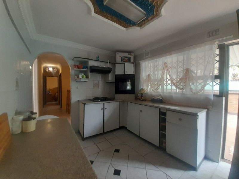 A dated kitchen featuring built-in cabinetry, an integrated oven, and hob, with direct access to an outdoor area through a security gate.