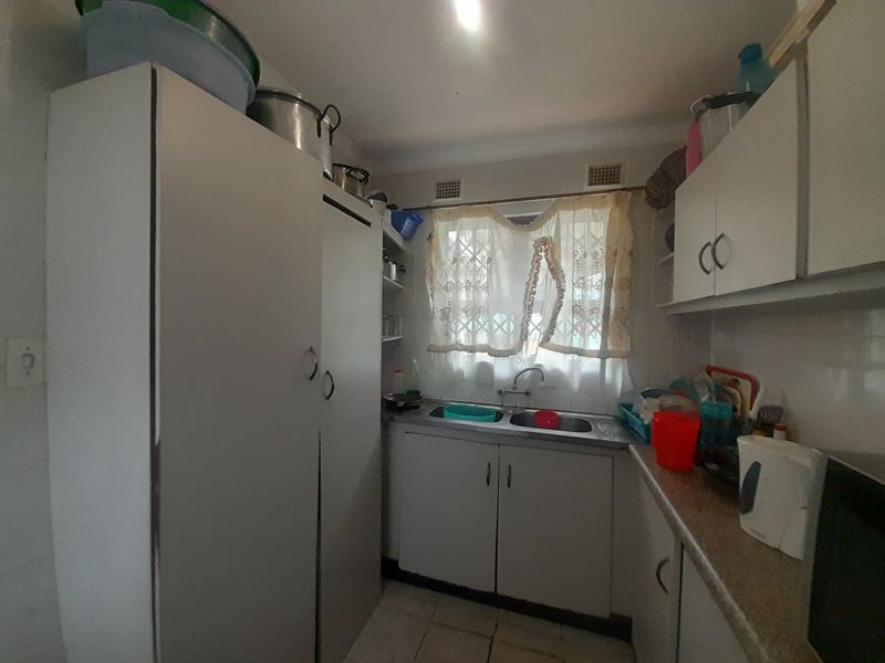 A compact kitchen featuring built-in cabinetry, laminate countertops, and a double basin sink, offering a functional layout with potential for modernization.