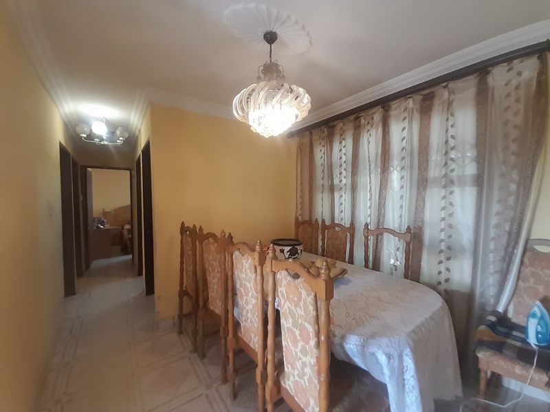 A dining room featuring tiled flooring, decorative ceiling cornice, and a central chandelier, with an adjacent hallway leading to other rooms.