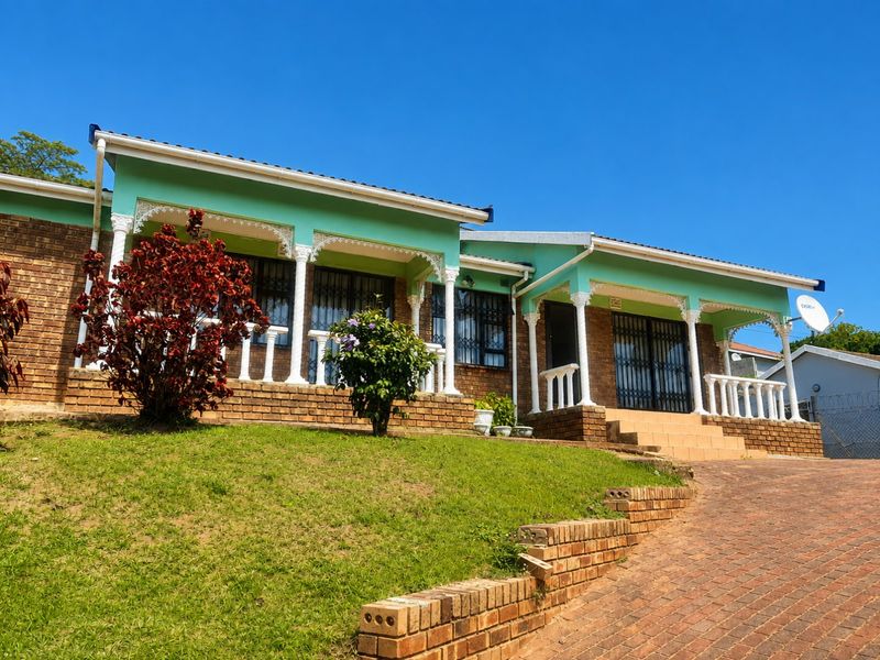 Front elevation of a brick house featuring a covered veranda with decorative columns, a paved driveway, and a landscaped front lawn.