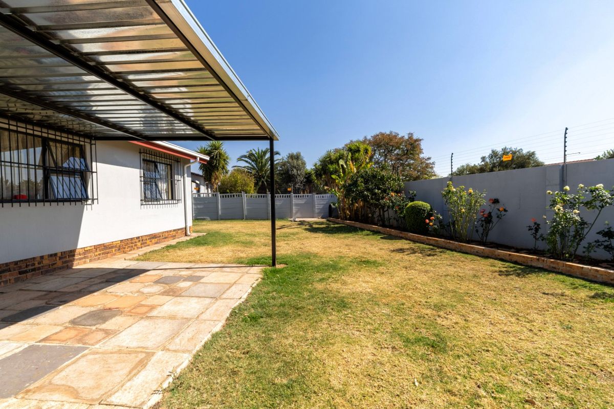 A rear garden featuring a paved patio area with a metal roof covering, enclosed by a perimeter wall with electric fencing.