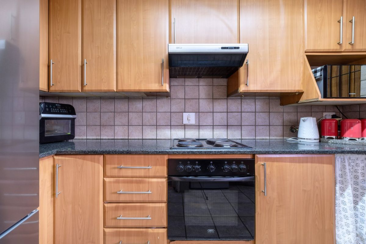 A functional kitchen featuring wood-look laminate cabinetry, granite countertops, a tiled backsplash, and integrated electric cooking appliances.