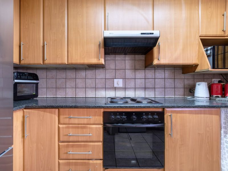 A functional kitchen featuring wood-look laminate cabinetry, granite countertops, a tiled backsplash, and integrated electric cooking appliances.