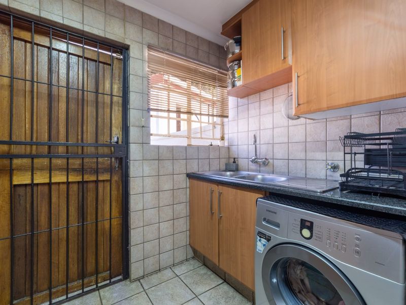 Functional laundry area featuring built-in wooden cabinetry, stainless steel sink, tiled splashback, and direct access to the exterior via a secure wooden door.