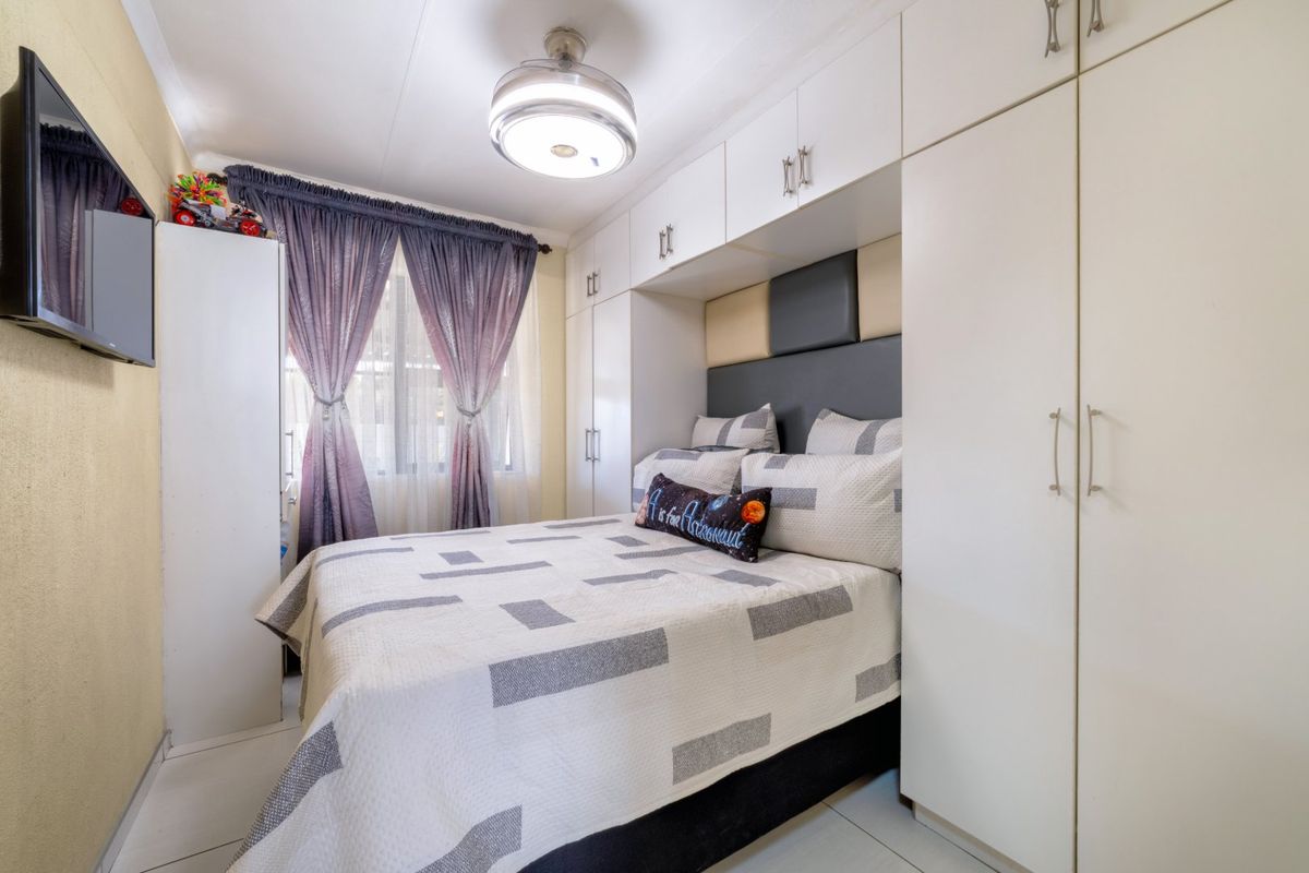 A well-maintained bedroom featuring extensive built-in cupboards with overhead storage, tiled flooring, and a central ceiling light fixture.