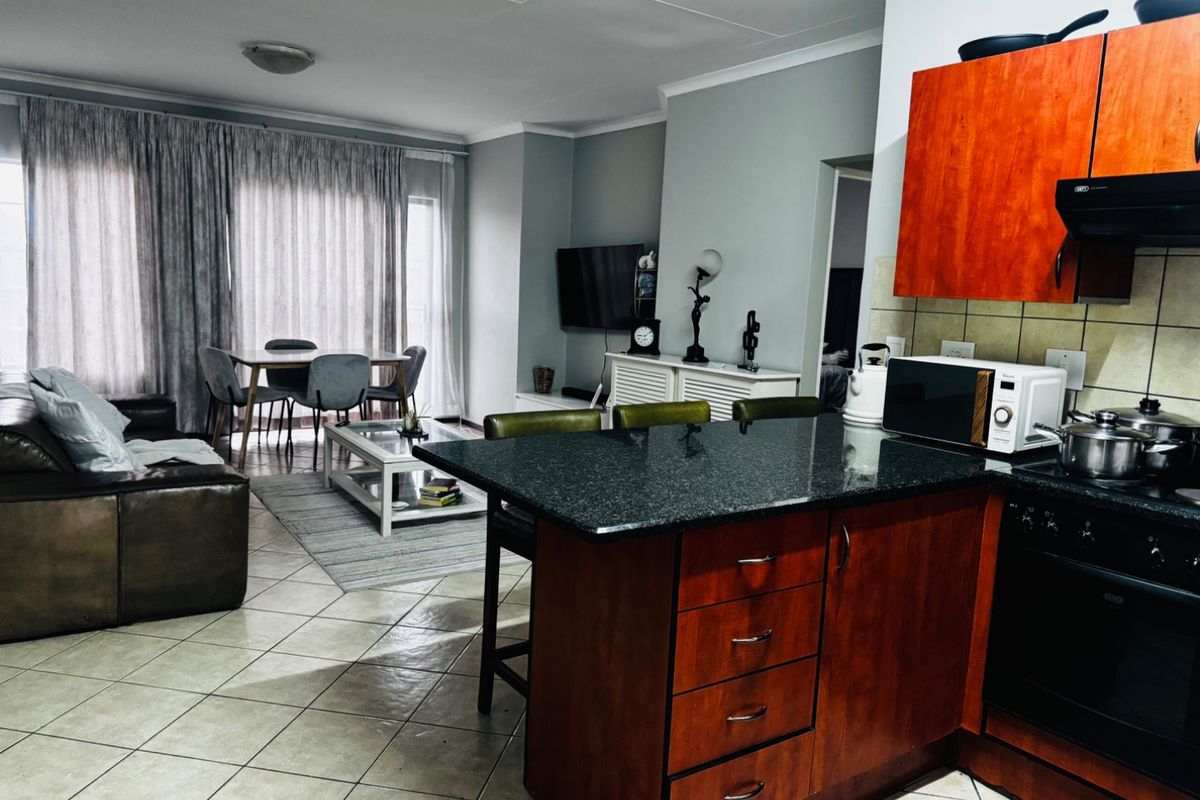 Open-plan living area featuring a kitchen with granite countertops and wooden cabinetry, flowing into a dining and lounge space with tiled flooring.