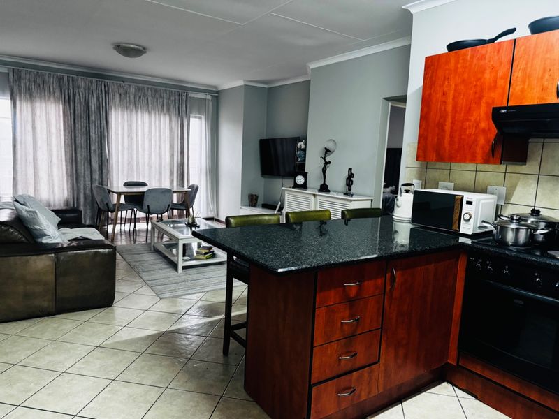 Open-plan living area featuring a kitchen with granite countertops and wooden cabinetry, flowing into a dining and lounge space with tiled flooring.