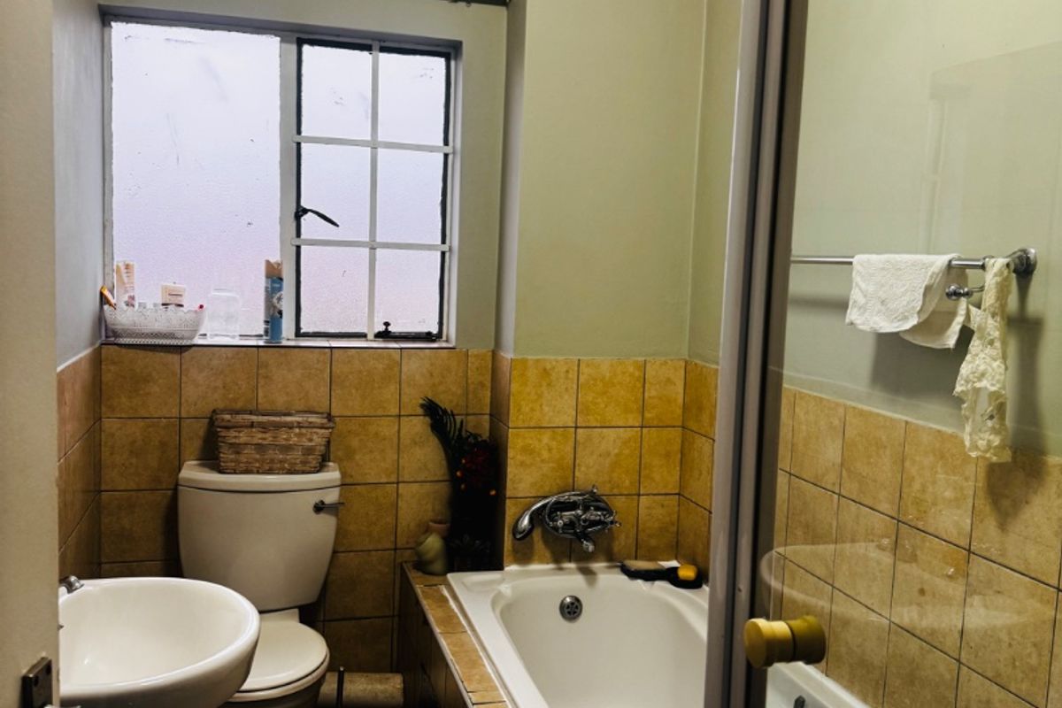 A functional bathroom featuring a pedestal basin, toilet, and a built-in bathtub with a shower screen and tiled splashback.
