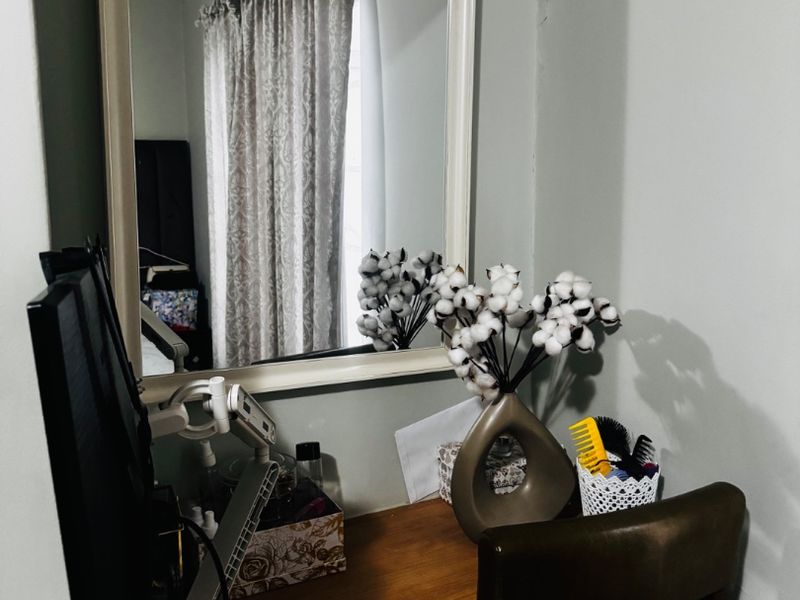 A bedroom corner featuring a wall-mounted mirror and curtain track, currently utilized as a small workspace area.