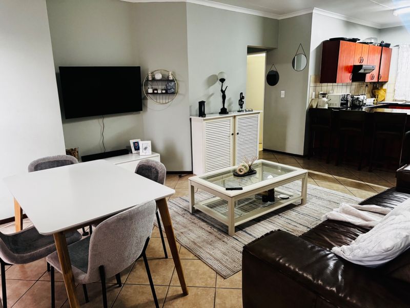 Open-plan living and dining area featuring tiled flooring and an adjacent kitchen with built-in cabinetry and a tiled backsplash.