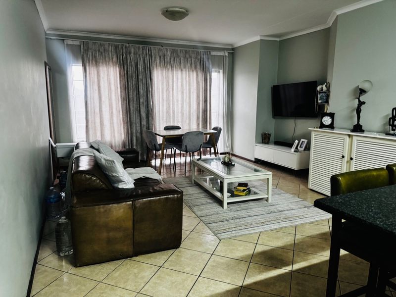 An open-plan living and dining area featuring tiled flooring, neutral wall tones, and large windows with floor-to-ceiling curtains.