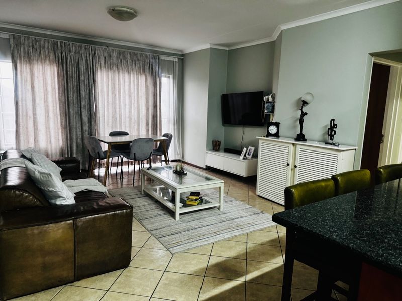 An open-plan living and dining area featuring tiled flooring, coved ceilings, and a functional layout with a granite-topped breakfast bar.