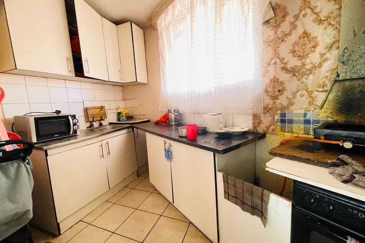 A dated kitchen featuring built-in cabinetry, tiled backsplash, and ceramic flooring, currently requiring significant cosmetic updates and renovation to improve its overall condition.