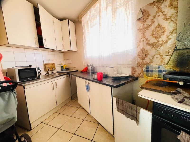 A dated kitchen featuring built-in cabinetry, tiled backsplash, and ceramic flooring, currently requiring significant cosmetic updates and renovation to improve its overall condition.