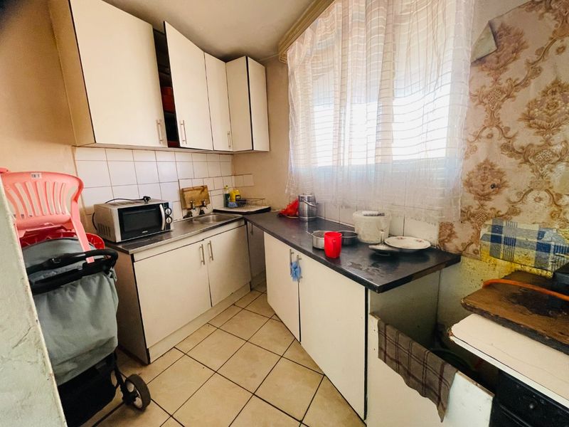 A compact kitchen featuring dated cabinetry, tiled flooring, and a tiled backsplash, offering significant potential for modernization and renovation.