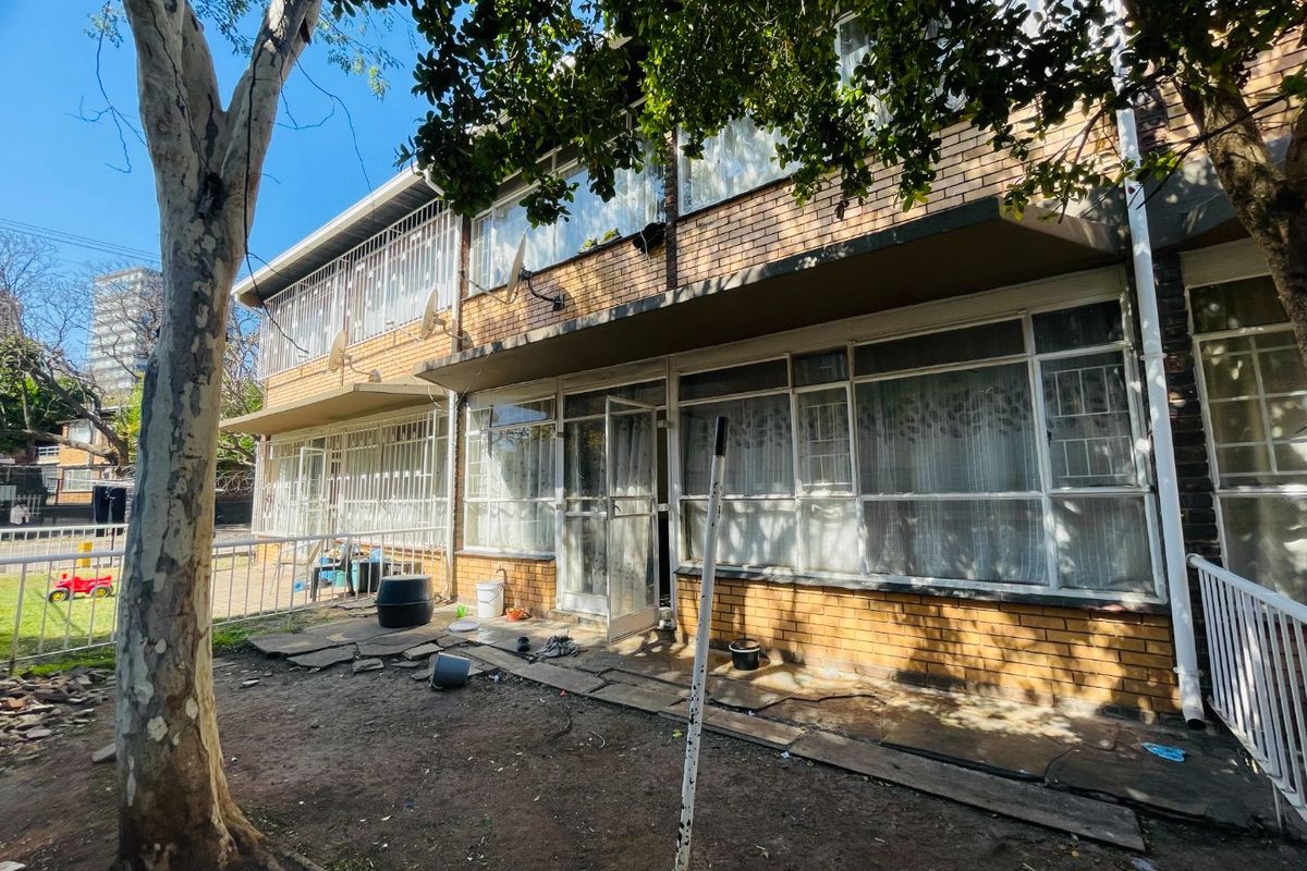 Rear view of a brick apartment building featuring ground floor access with security bars and a small paved patio area.