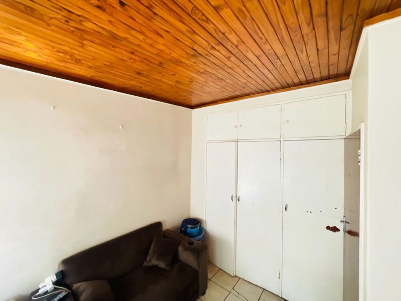 Bedroom featuring built-in cupboards, tiled flooring, and a wooden ceiling. The space requires cosmetic updates to the cabinetry and wall finishes.