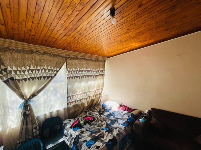 A bedroom featuring a distinctive timber tongue and groove ceiling and large window with curtain tracks.