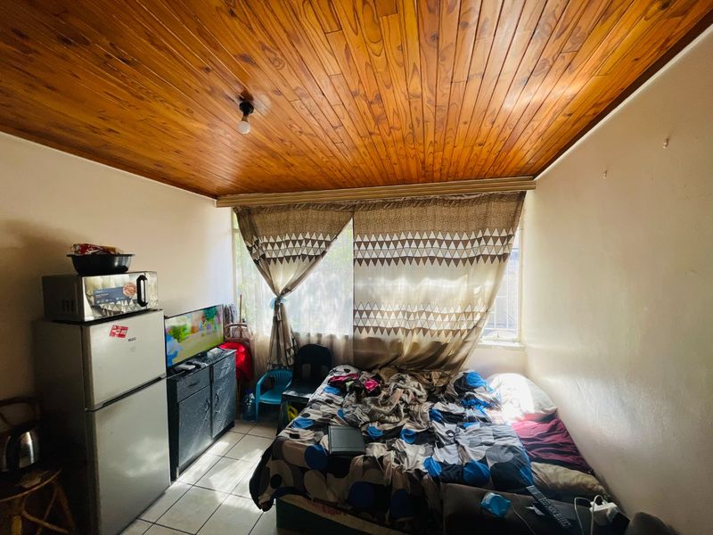 A compact bedroom featuring a timber tongue and groove ceiling, tiled flooring, and a large window providing natural light.
