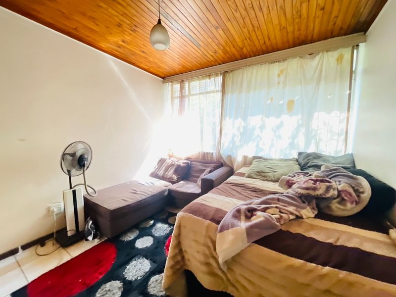 A bedroom featuring a timber tongue and groove ceiling, tiled flooring, and a pendant light fixture, requiring cosmetic updates to improve its overall condition.