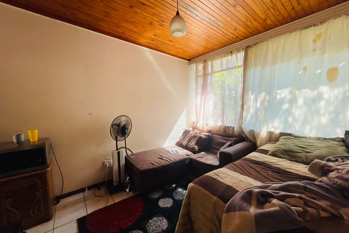A bedroom featuring a warm timber tongue and groove ceiling, tiled flooring, and a large window allowing natural light into the space.