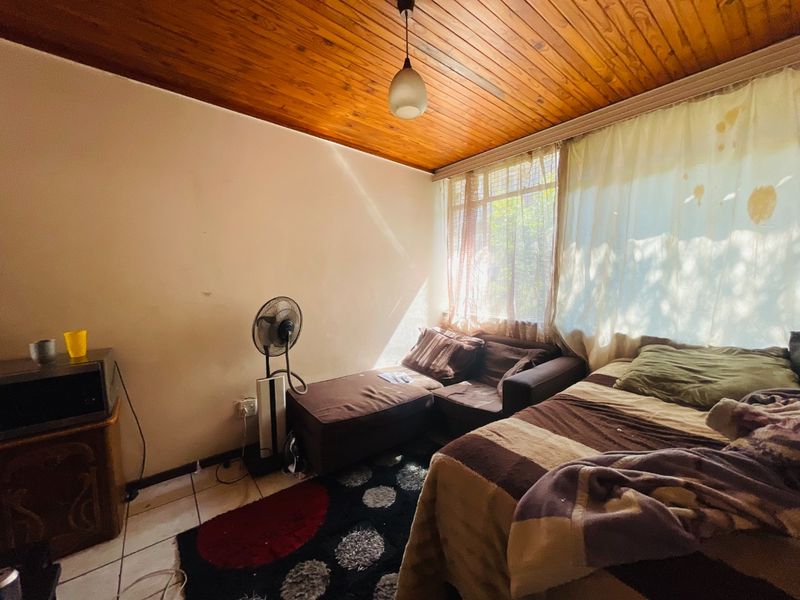 A bedroom featuring a warm timber tongue and groove ceiling, tiled flooring, and a large window allowing natural light into the space.