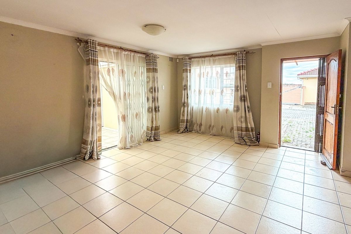 Spacious, light-filled living area featuring neutral tiled flooring, coved ceilings, and direct access to the exterior through a sliding glass door.