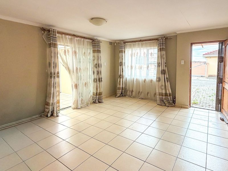 Spacious, light-filled living area featuring neutral tiled flooring, coved ceilings, and direct access to the exterior through a sliding glass door.