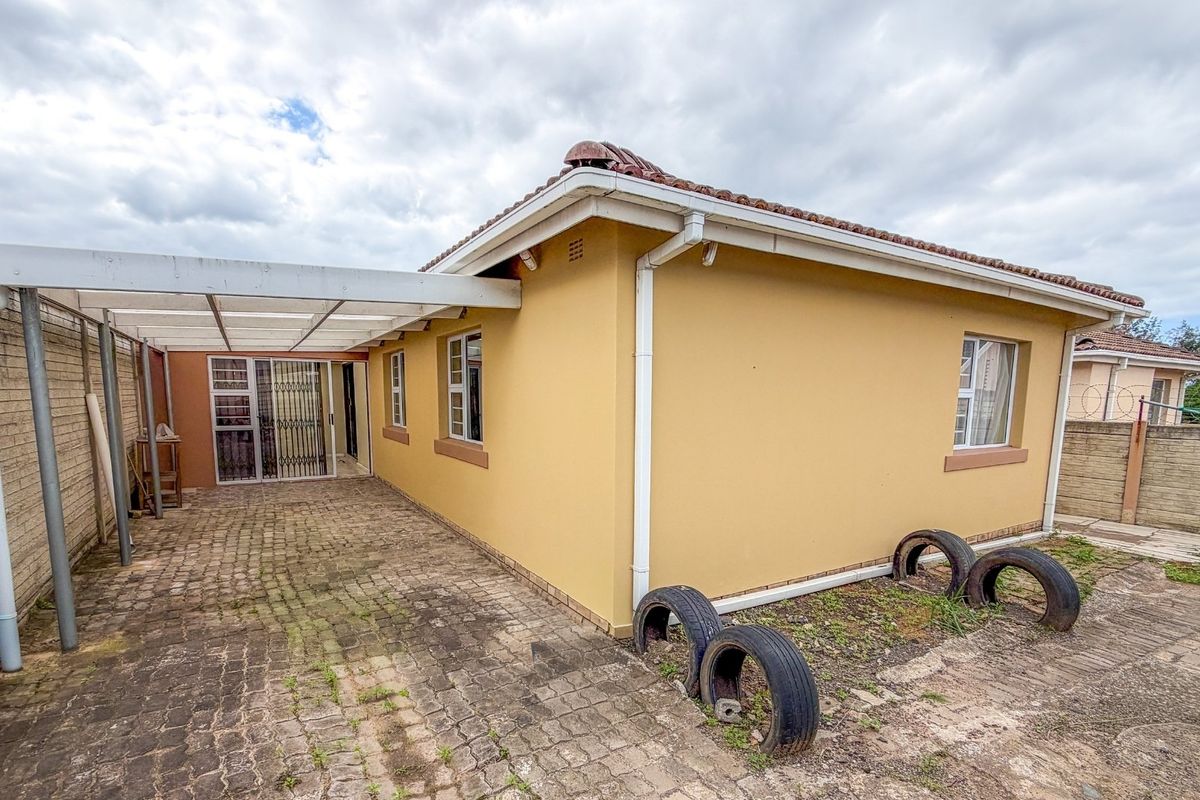 Rear exterior view of the property featuring a paved driveway, covered carport, and perimeter boundary walling.